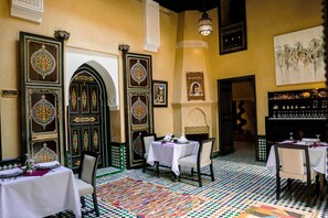 A dining area with tables set for service, ornate doors, and a patterned floor.