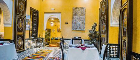 A dining area with a checkered floor, a table set for two, and ornate wall decorations.