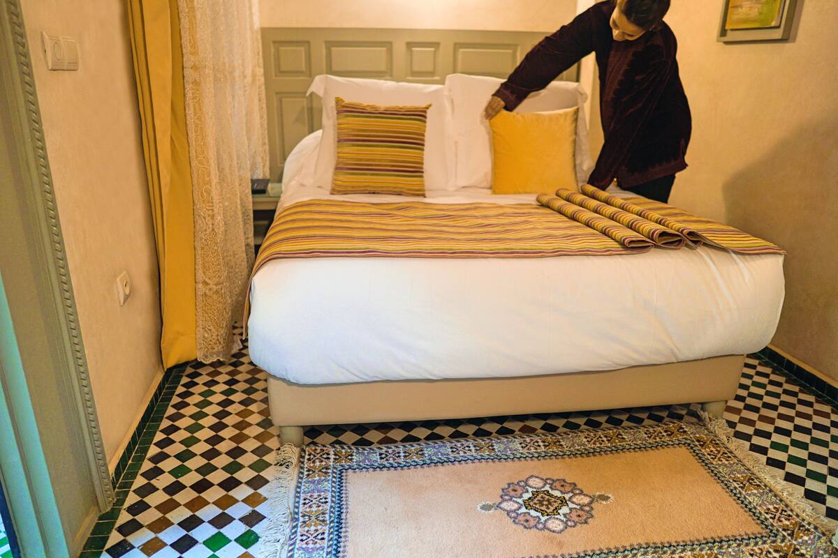 A neatly made bed with striped bedding, a patterned rug, and a checkered floor.