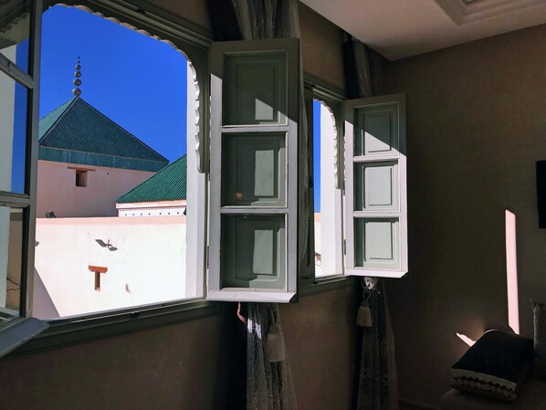 Una habitación con ventana abierta que muestra un edificio con techo verde y pared rosa.