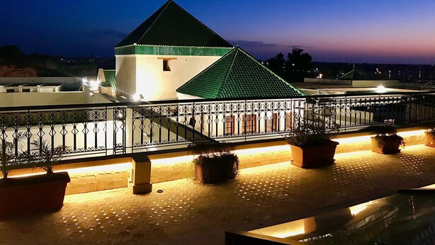 A building with a green roof and white walls, surrounded by a metal railing and potted plants. - Riad Zidania (Meknes)