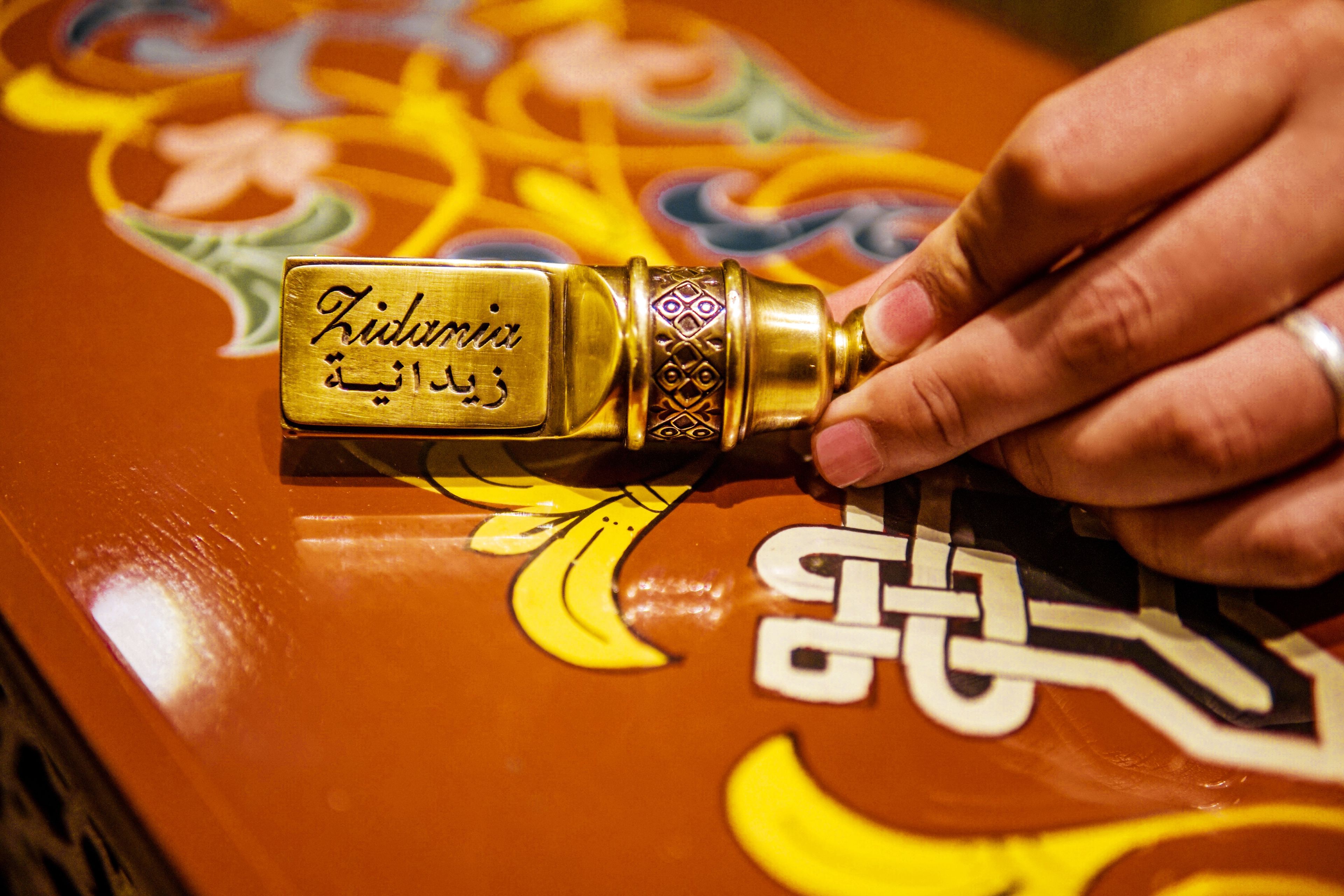 Een hand houdt een bronzen sleutel met Arabische inscripties vast, op een tafel met een kleurrijk, gedetailleerd patroon.