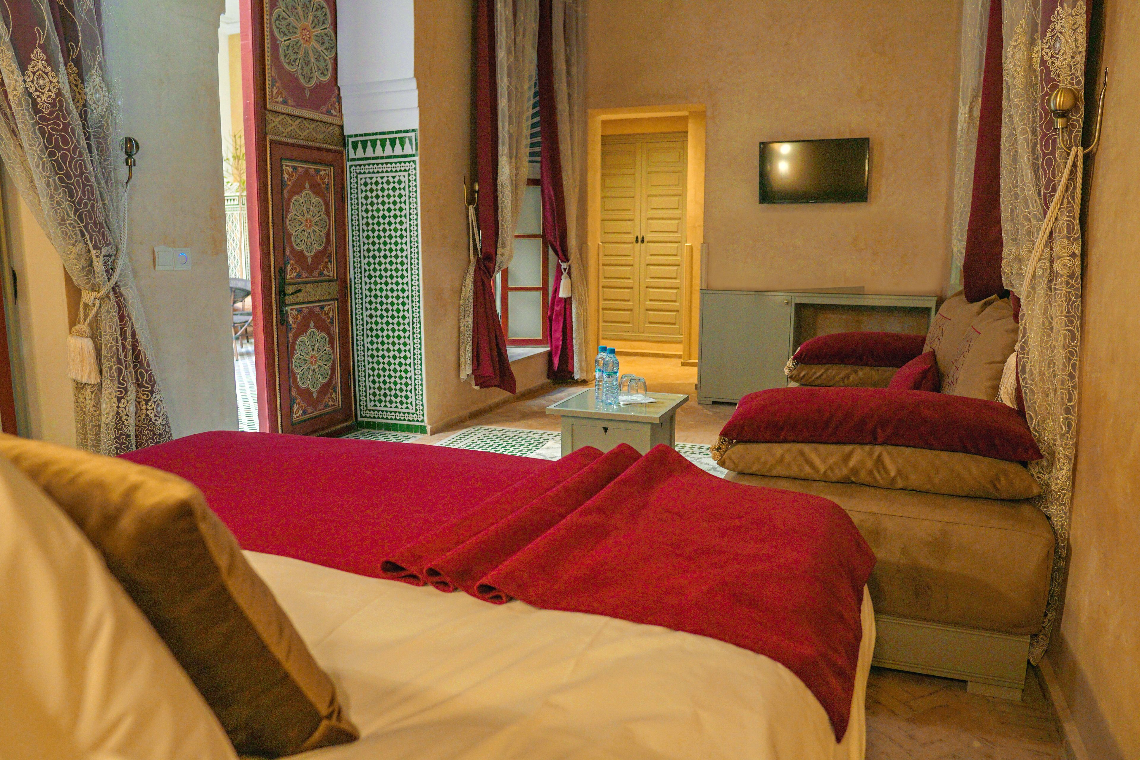 Ein Hotelzimmer mit einem Bett, einem Sofa, einem kleinen Tisch mit einer Wasserflasche und einem an der Wand befestigten Fernseher.