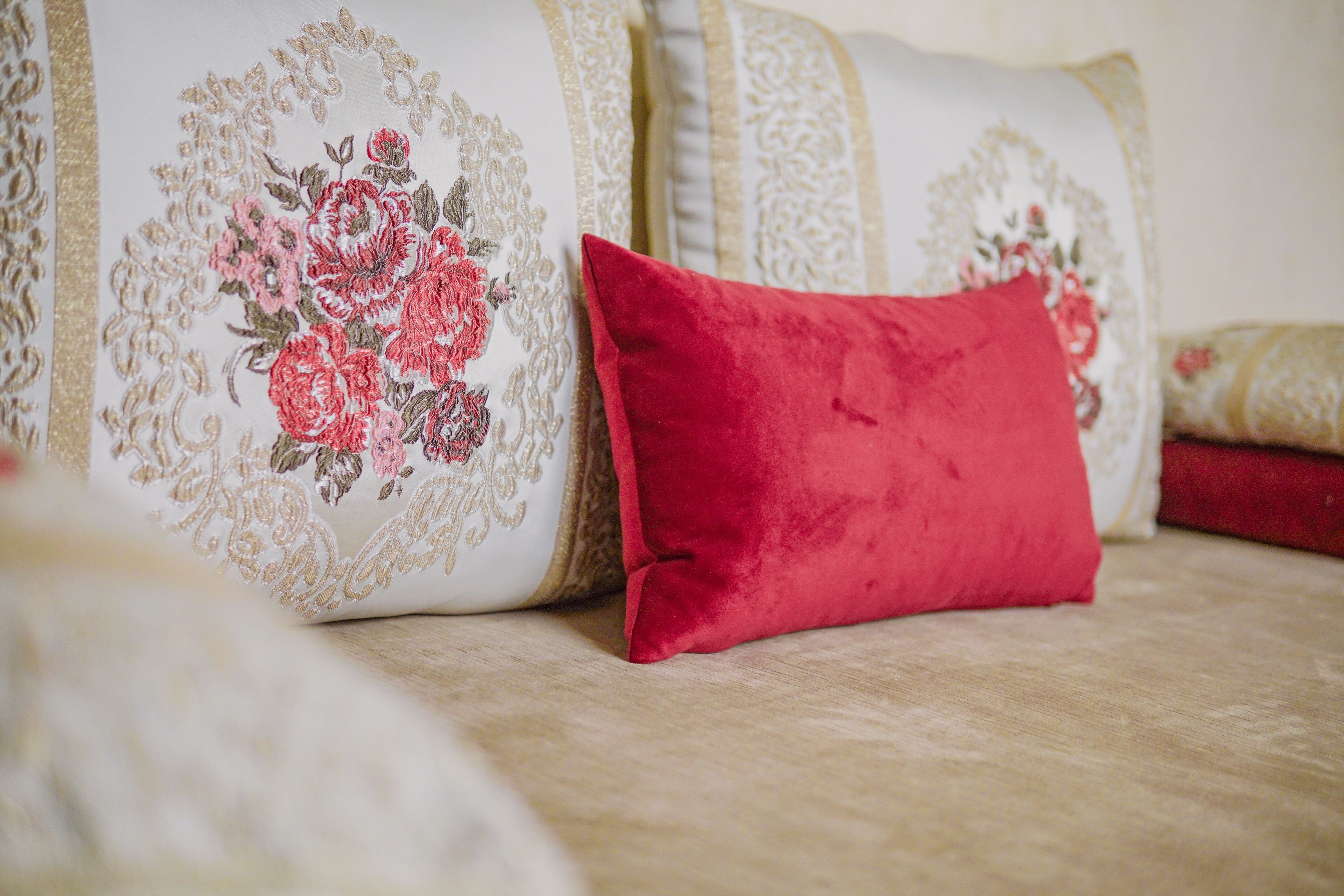 A bed with a floral-patterned pillow and a solid red pillow.