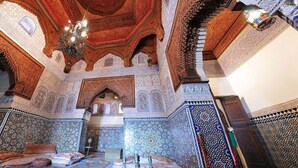 An ornate room with intricate tile work, a chandelier, and a bed with pillows. - Riad Zidania (Meknes)