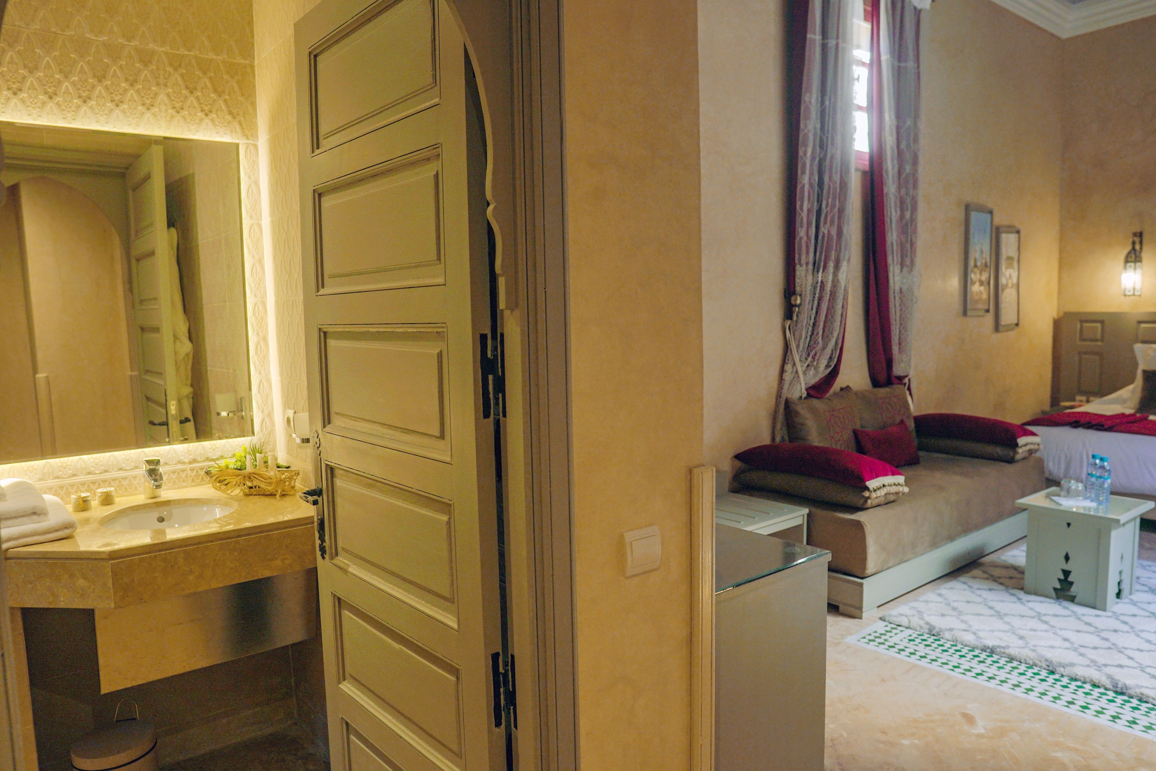 A hotel room with a bathroom, a bed, a bedside table, and a nightstand.