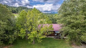 A rural house with a red roof, surrounded by lush greenery and trees. - Deep Creek Log Cabin- Motorcycle Friendly - Gas Fireplace - Covered Porch (Bryson City)