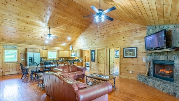 A spacious living room with a leather sofa, a fireplace, a television, and a stone fireplace surround. - Deep Creek Log Cabin- Motorcycle Friendly - Gas Fireplace - Covered Porch (Bryson City)