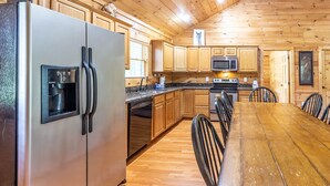 A kitchen with wooden cabinets, a stainless steel refrigerator, a microwave, and a dining table with chairs. - Deep Creek Log Cabin- Motorcycle Friendly - Gas Fireplace - Covered Porch (Bryson City)