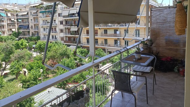 Un balcon avec une table et une chaise, donnant sur un quartier résidentiel composé de plusieurs immeubles et d’espaces verts.