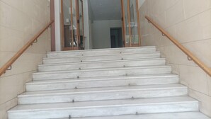 Un escalier aux marches blanches et aux rampes en bois, menant à une pièce dotée d’une porte en verre et offrant une vue sur une autre pièce.