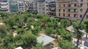 Un immeuble résidentiel à plusieurs étages, doté de balcons, d’une cour intérieure avec des arbres et d’un petit espace extérieur aménagé pour s’asseoir.