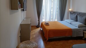 Un dormitorio con cama, escritorio, estante con libros y ventana con cortinas.