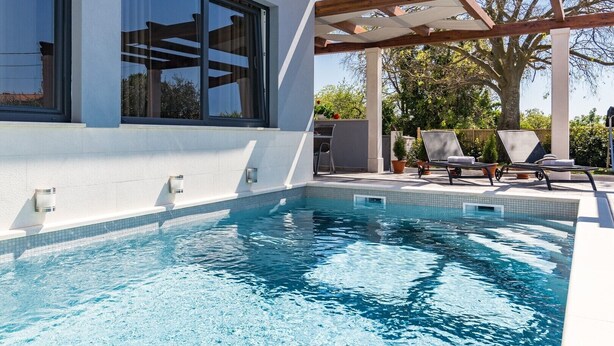 A swimming pool with a pergola and lounge chairs, surrounded by a white building with large windows. - Villa Sunny Home in Galizana (Galizana)