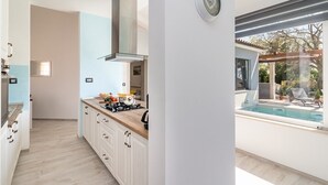 A modern kitchen with a gas stove, cabinets, and a view of a swimming pool. - Villa Sunny Home in Galizana (Galizana)