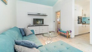 A modern living room with a teal sofa, a flat-screen TV, a glass coffee table, and a colorful bench. - Villa Sunny Home in Galizana (Galizana)