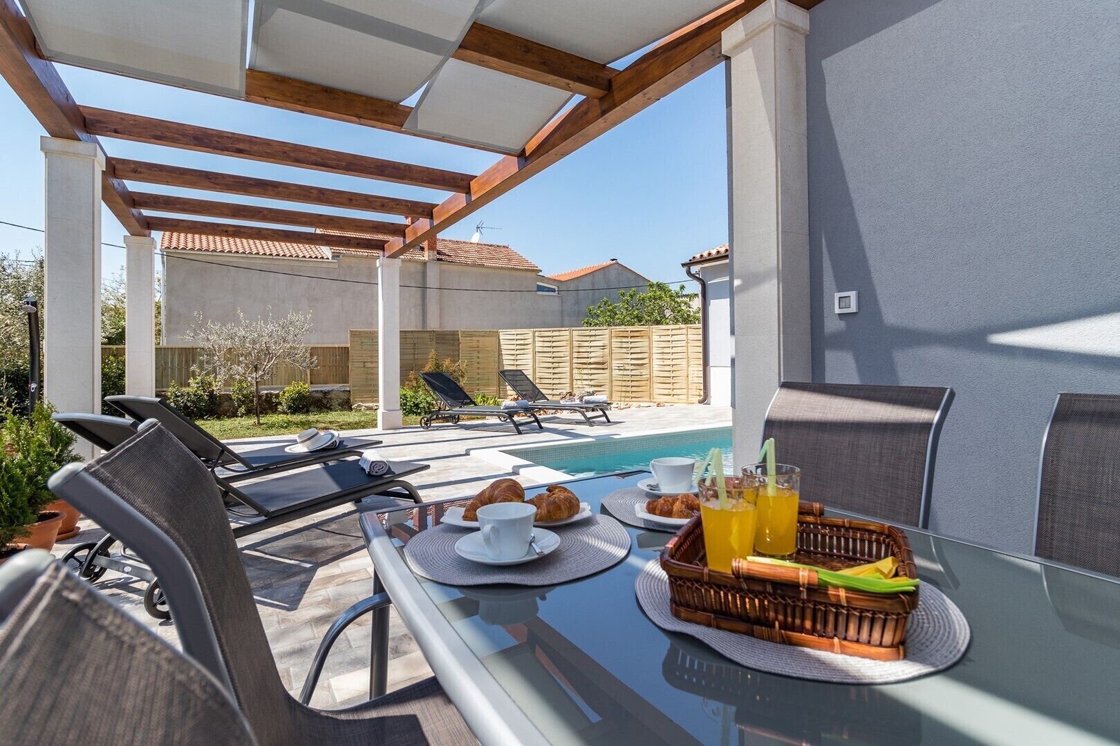 Un espace extérieur aménagé, abrité et doté d’une piscine, de chaises longues et d’une table où sont disposés des éléments pour le petit-déjeuner.