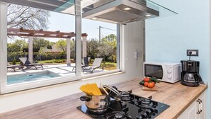 A modern kitchen with a glass enclosure, a built-in stove, a microwave, and a coffee maker. - Villa Sunny Home in Galizana (Galizana)