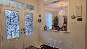 A hallway with a double door featuring stained glass, a chandelier, a mirror reflecting a dining area, and a doormat. - A BEAUTIFUL & SPACIOUS 4 BEDROOM VACATION HOME (Niagara Falls)