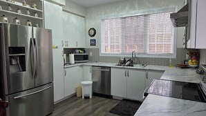 A modern kitchen with stainless steel appliances, white cabinetry, a marble countertop, and a window with blinds. - A BEAUTIFUL & SPACIOUS 4 BEDROOM VACATION HOME (Niagara Falls)