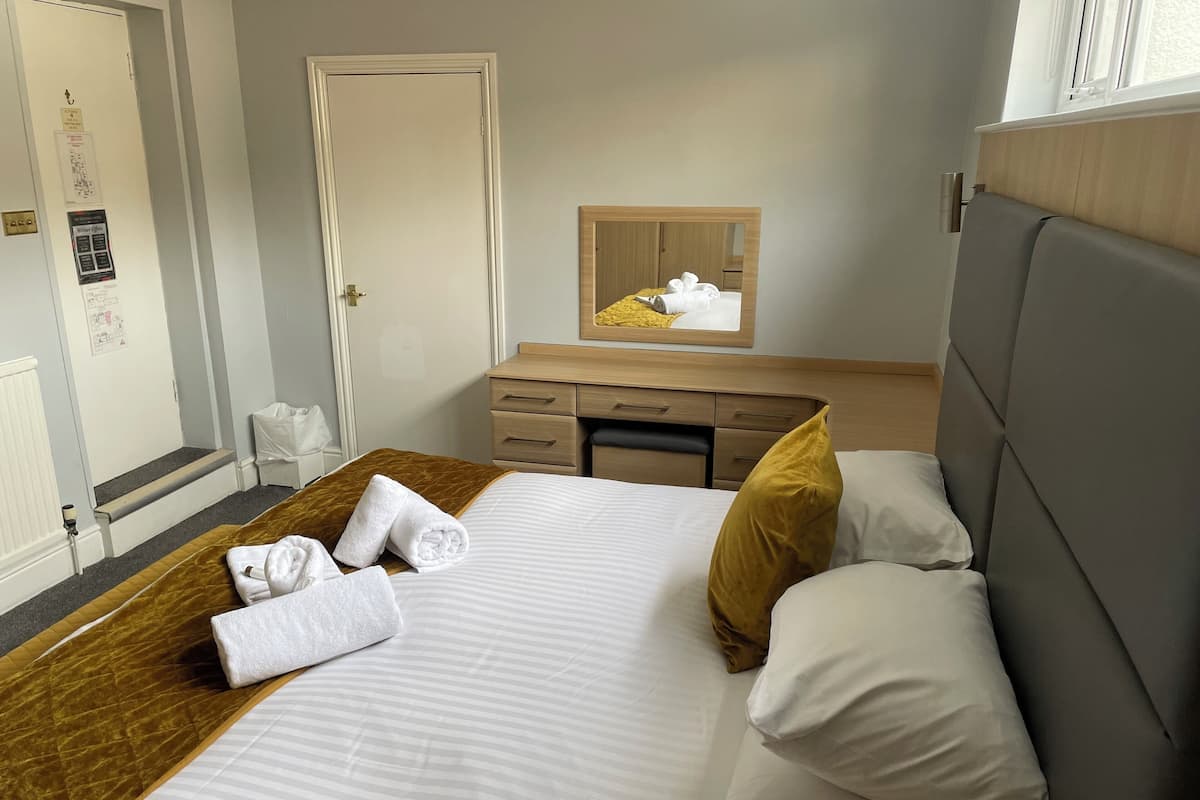 Hotellihuone, jossa on sänky, puinen yöpöytä, työpöytä ja peili.