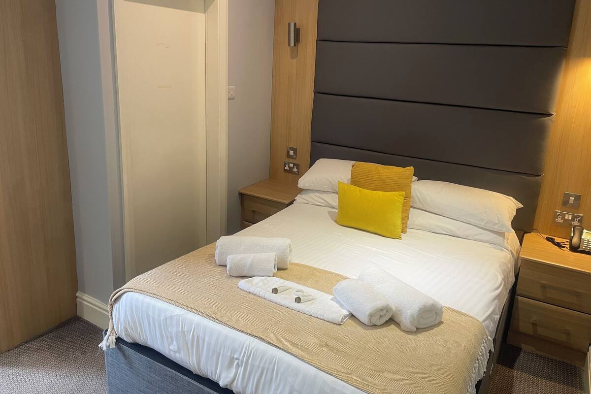Hotellihuone, jossa on sänky, kaksi yöpöytää, puinen vaatekaappi ja ovi.