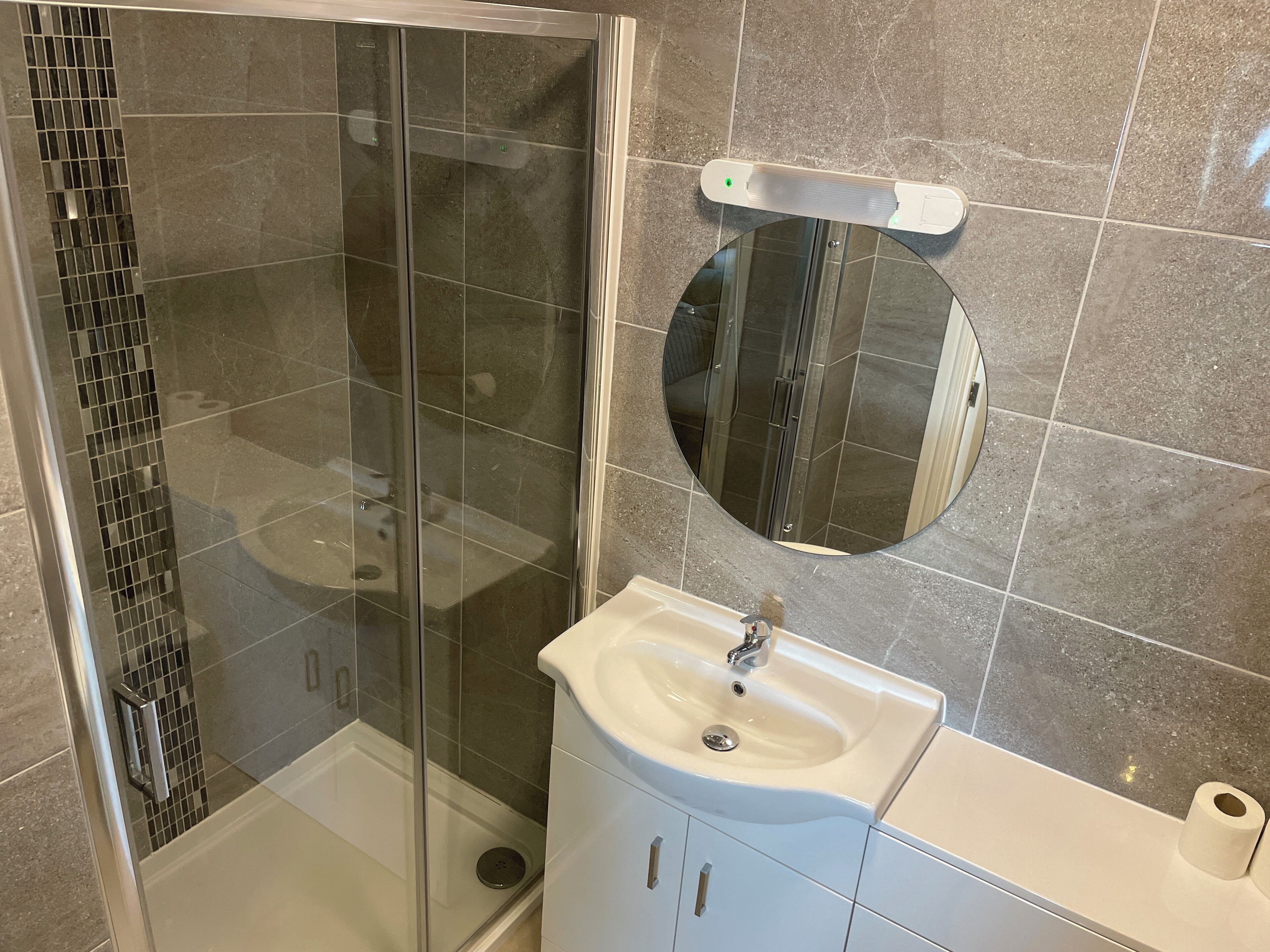 A modern bathroom with a glass-enclosed shower, a white sink, and a mirror above it.