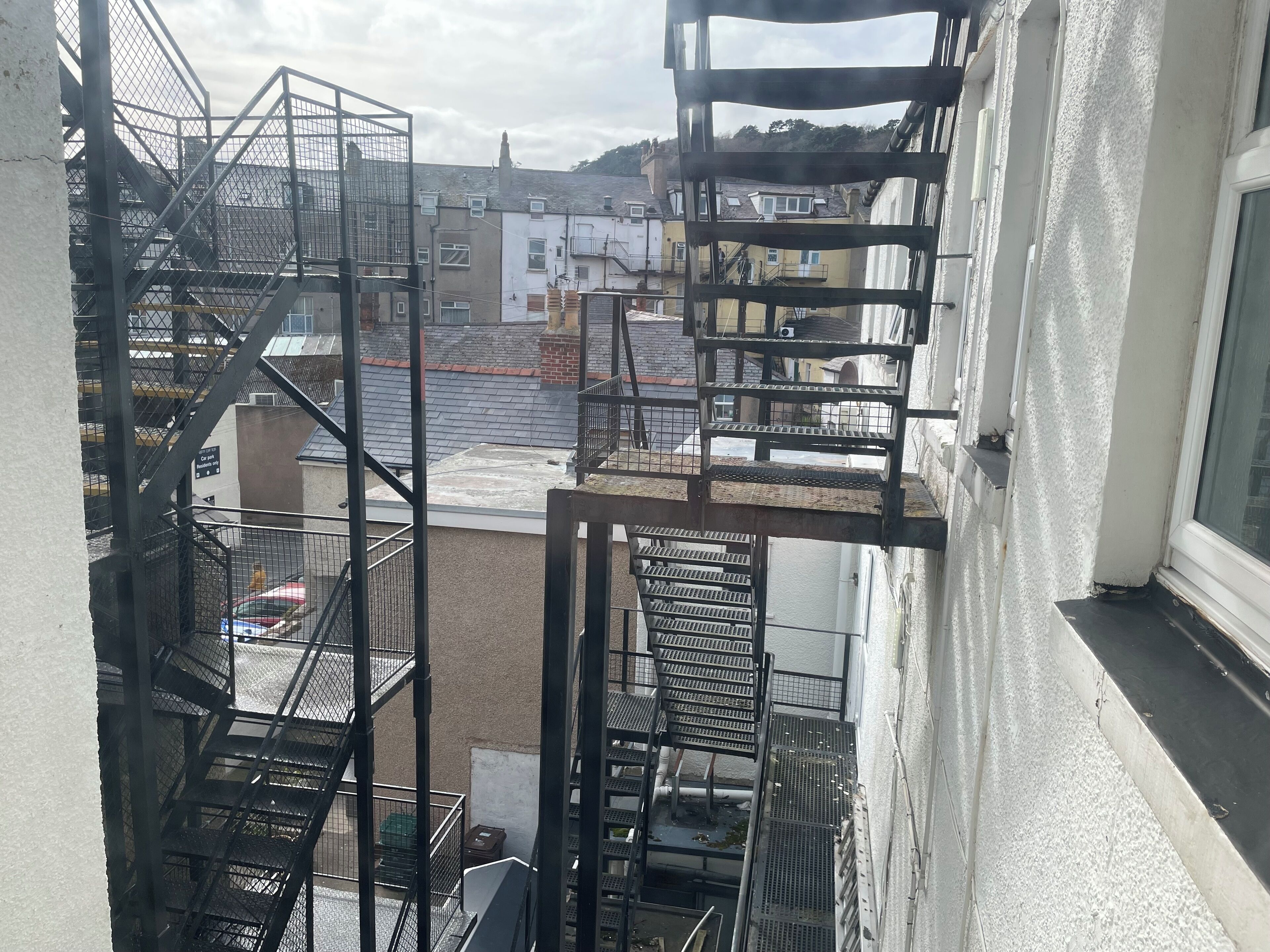 A view from a window overlooking a building with multiple fire escape staircases and a street below.
