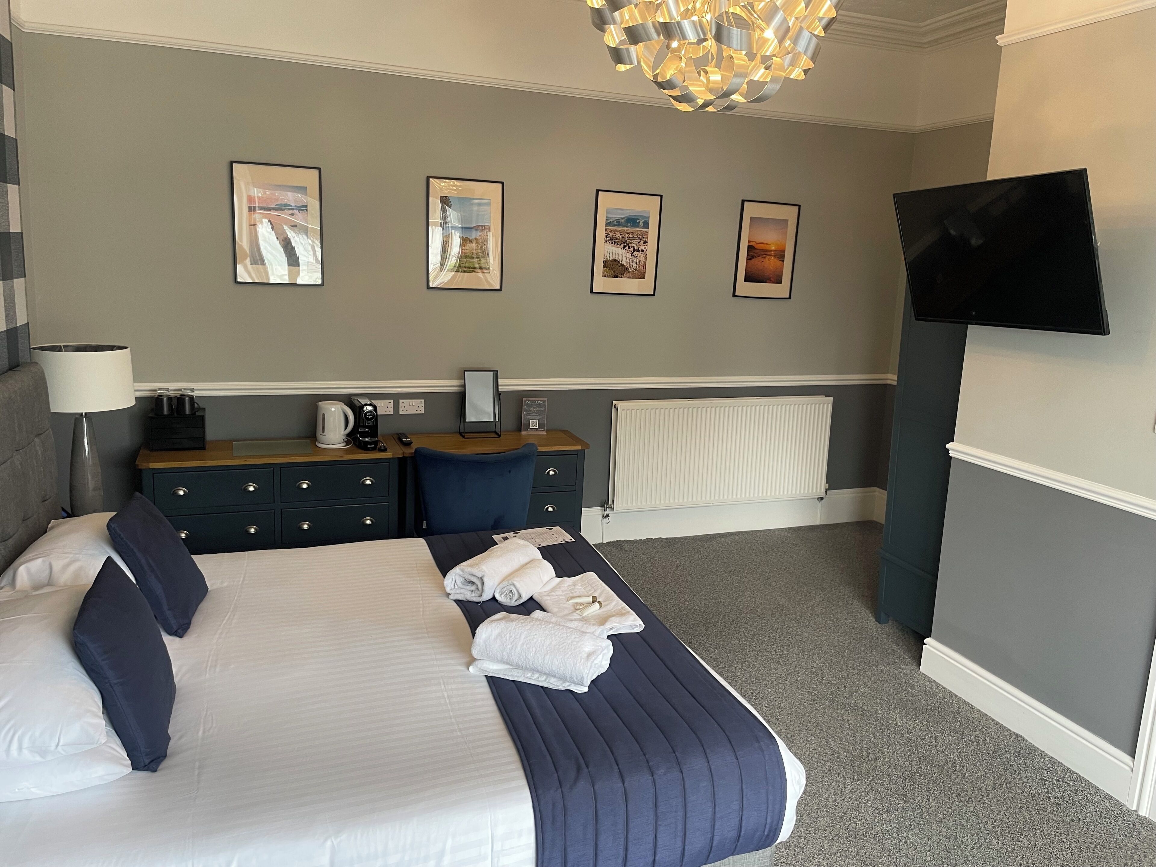 Ein Hotelzimmer mit Bett, Schreibtisch, Stuhl, Lampe, Fernseher und gerahmten Bildern an der Wand.