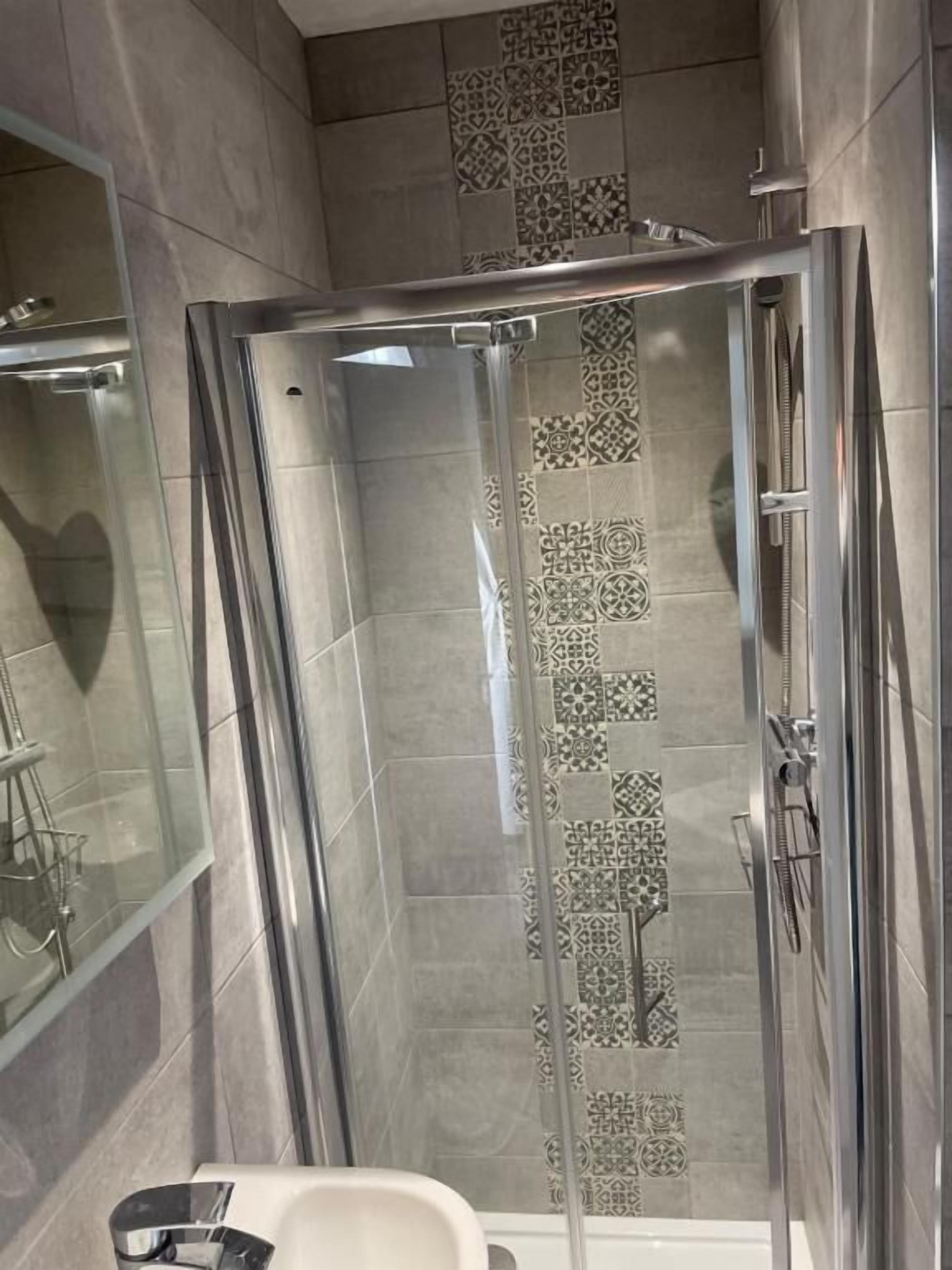 A modern bathroom with a glass-enclosed shower, a white sink, and a mirror.