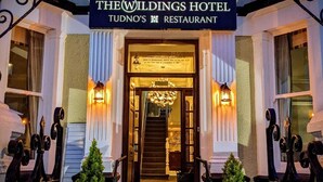 The Wildings Hotel Tudno's Restaurant with a classic entrance, a chandelier, and two potted plants at the steps. - The Wildings (Llandudno)