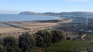 A coastal promenade with a pier extending into the sea, a promenade with benches, and a monument. - The Wildings (Llandudno)