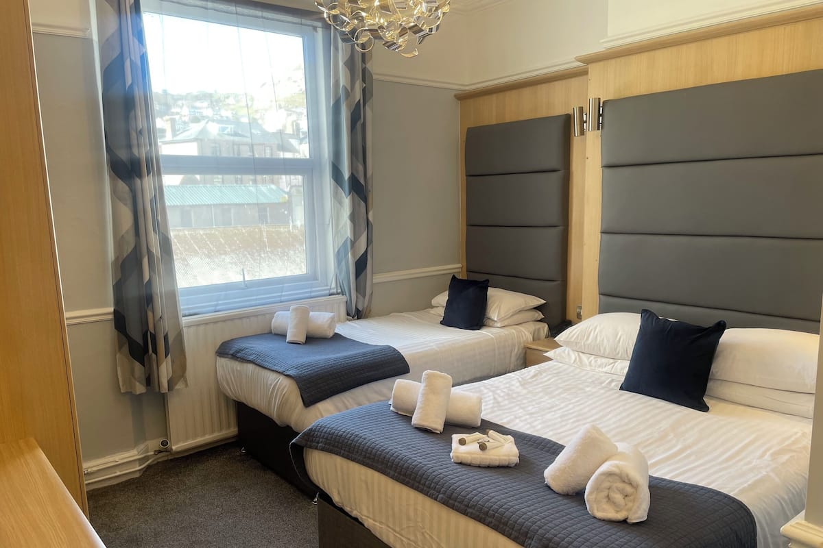 Hotellihuone, jossa on kaksi sänkyä, suuri ikkuna, jossa on verhot, kattokruunu ja näkymä ulos.