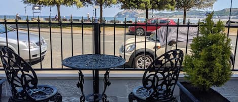 Ein Balkon mit zwei verzierten Metallstühlen und einem kleinen runden Tisch, mit Blick auf einen Parkplatz und ein Gewässer.