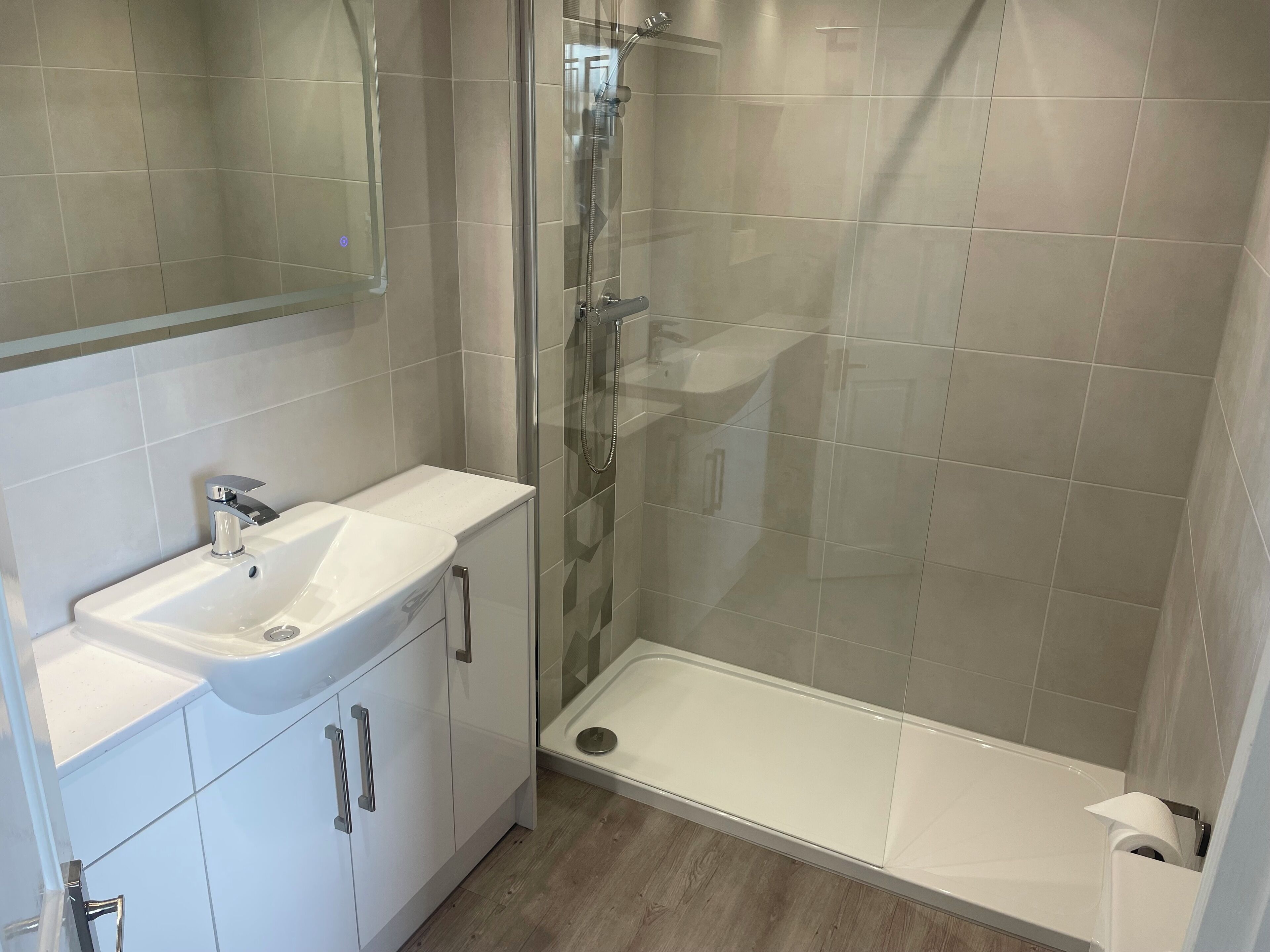 A modern bathroom with a glass-enclosed shower, a white sink, and a wooden floor.