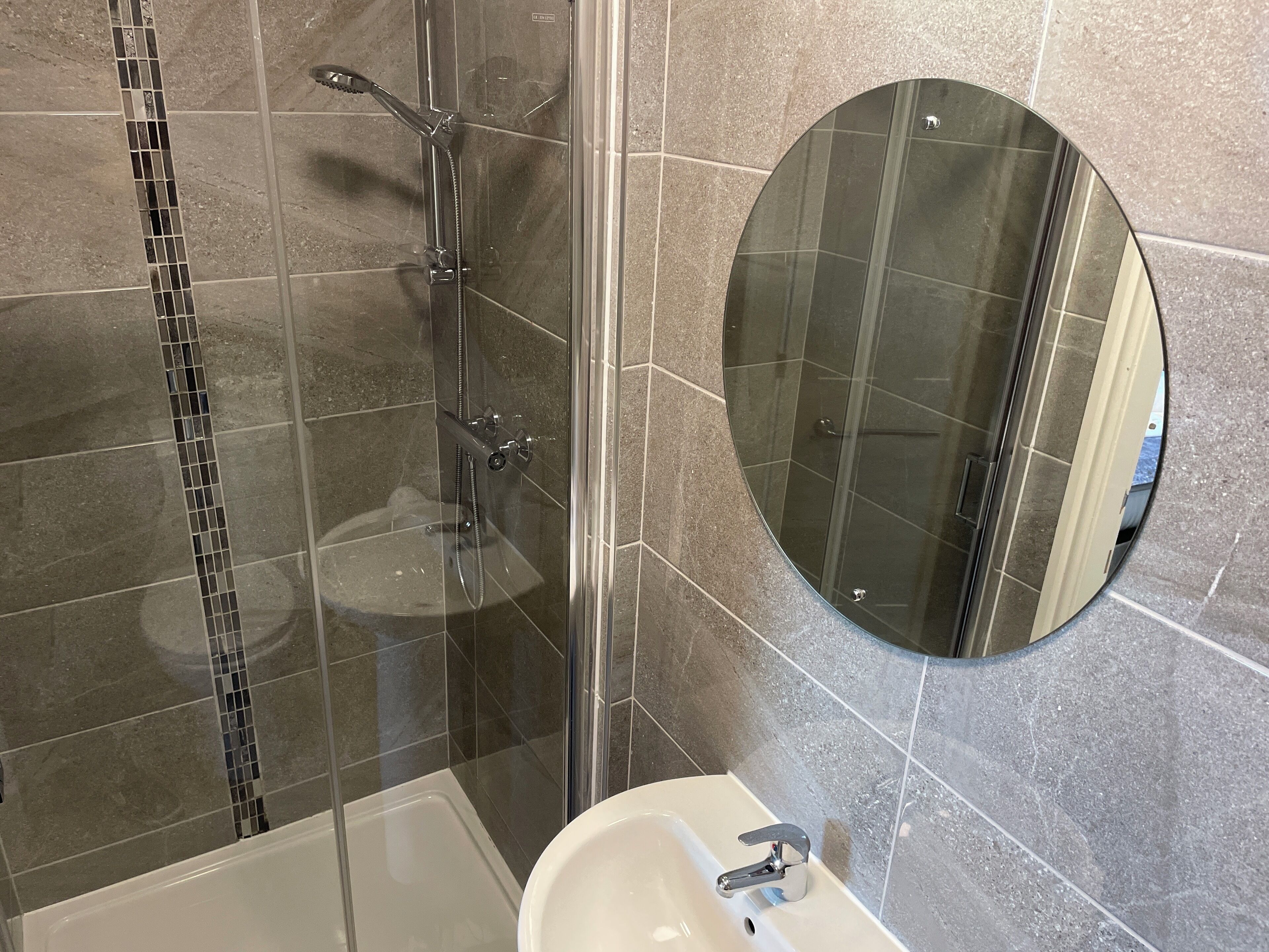 A modern bathroom with a glass-enclosed shower, a white sink, and a round mirror on the wall.