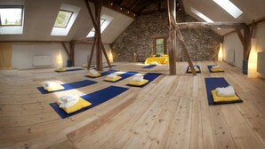 A spacious room with wooden floors, multiple yoga mats, and a stone wall. - Alpenretreat (Nassereith)