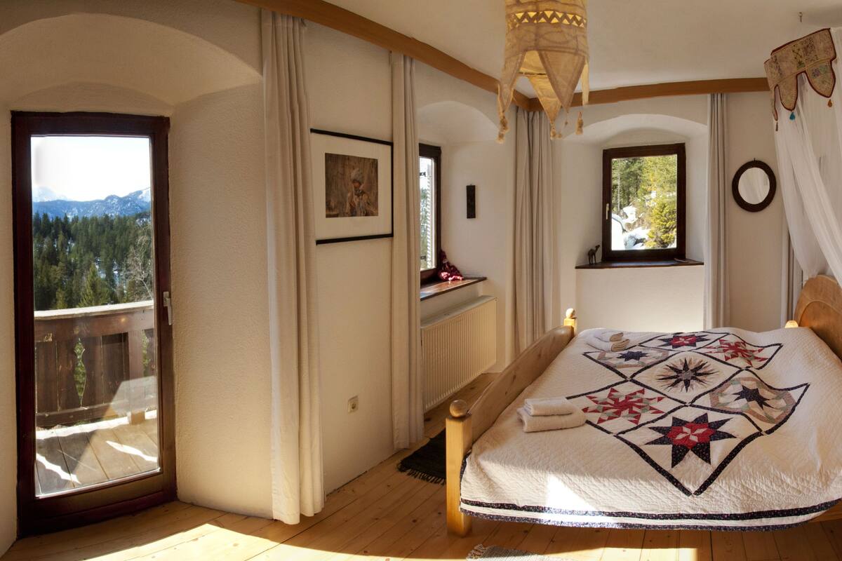 A bedroom with a large bed, a window with a view of mountains, and a balcony.