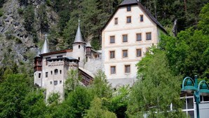 A castle-like building with multiple windows and a tower, surrounded by trees and a rocky hillside. - Alpenretreat (Nassereith)