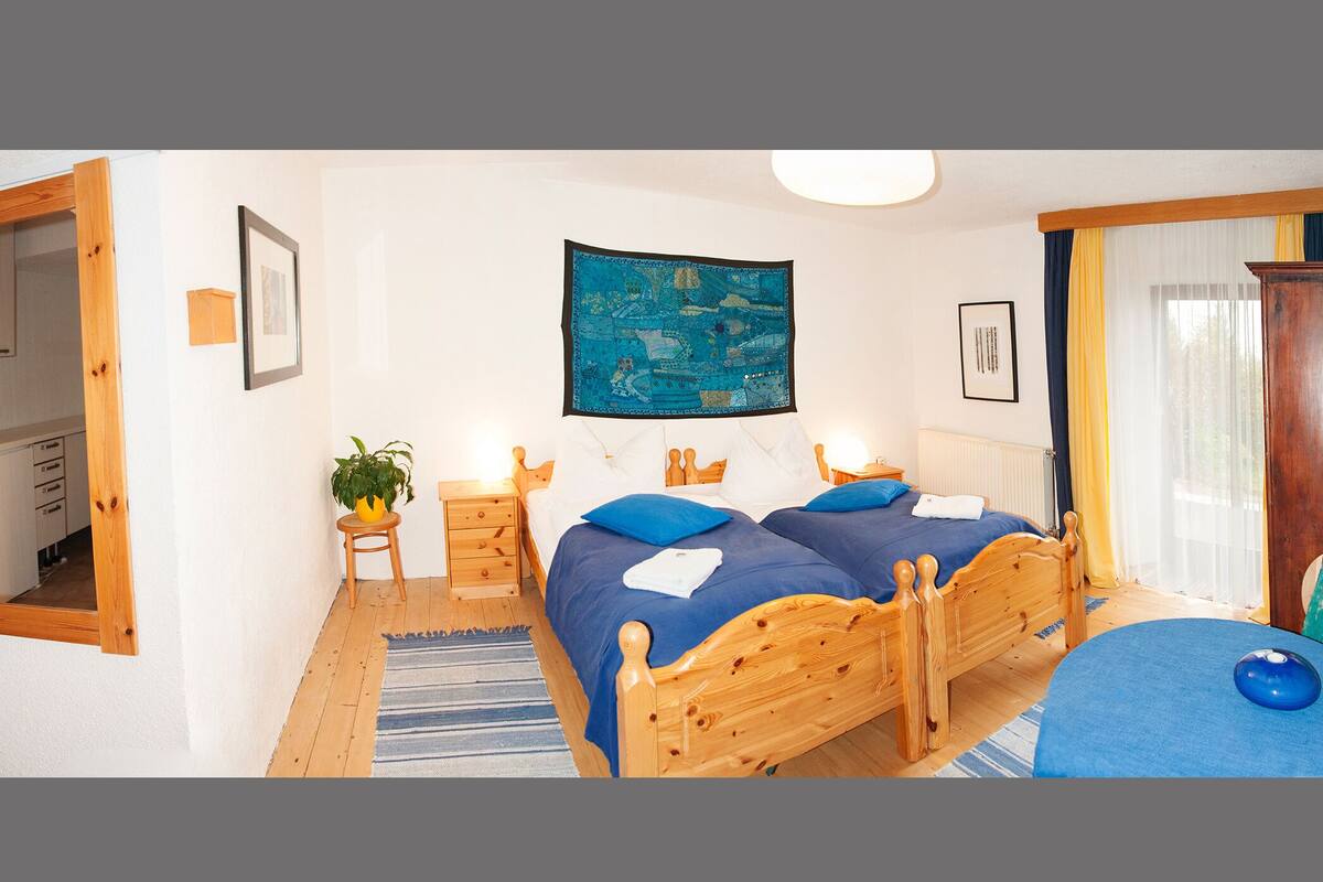 A bedroom with a wooden bed, two bedside tables, a nightstand, a wall-mounted painting, and a window with curtains.