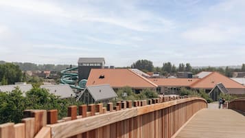 Une promenade en bois mène à un bâtiment doté d’un toboggan aquatique vert et d’un toit recouvert de tuiles rouges.