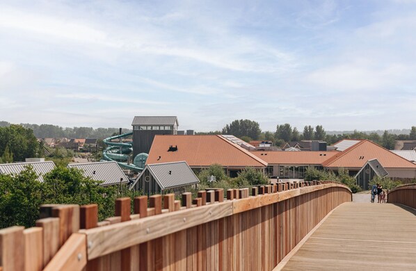 A wooden boardwalk leading to a building with a green water slide and a red-tiled roof.