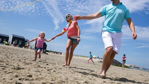 A beach scene with people holding hands and flying a kite.