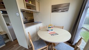 A compact kitchen with a dining area, wooden chairs, and a table with a magazine.