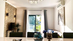 Un salón moderno con comedor, que incluye una pared de ladrillo, un ventanal con cortinas y un televisor de pantalla plana.