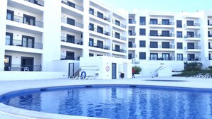 Un moderno edificio residencial de varios pisos con balcones, piscina y una pequeña zona de estar al aire libre.