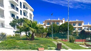 Un edificio residencial con varios balcones, un jardín bien cuidado con palmeras y un cielo azul despejado.