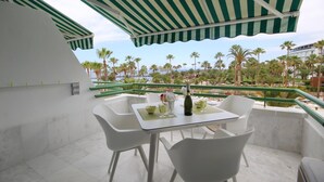 A balcony with a table set for two, overlooking a palm tree-lined view. - Luxury apartment on the first line of El Duque D11 (Costa Adeje)
