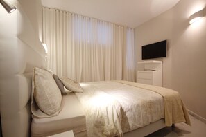 Un dormitorio con cama, cortinas, televisor y mesita de noche.