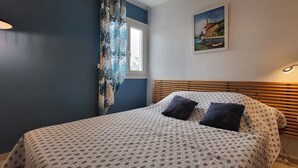 A bedroom with a bed, a window with curtains, a painting on the wall, and a bedside lamp. - Duplex with 3 rooms in a quiet neighbourhood (Var)
